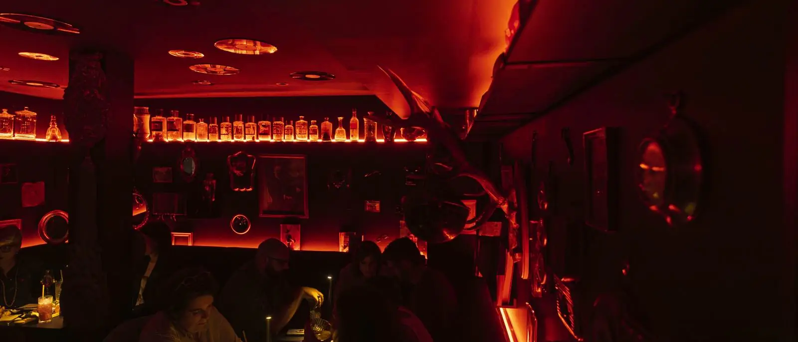 La Crypte, bar speakeasy de L'Arche : salle voûtée baignée de lumière rouge, miroirs et bouteilles rétro-éclairées