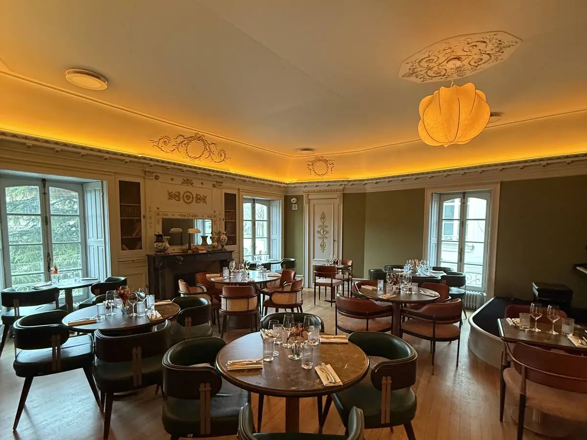 Le Grand Salon de L'Arche : corniches et médaillons en stuc, cheminée de marbre noir, bibliothèques vitrées, tables rondes et fauteuils verts