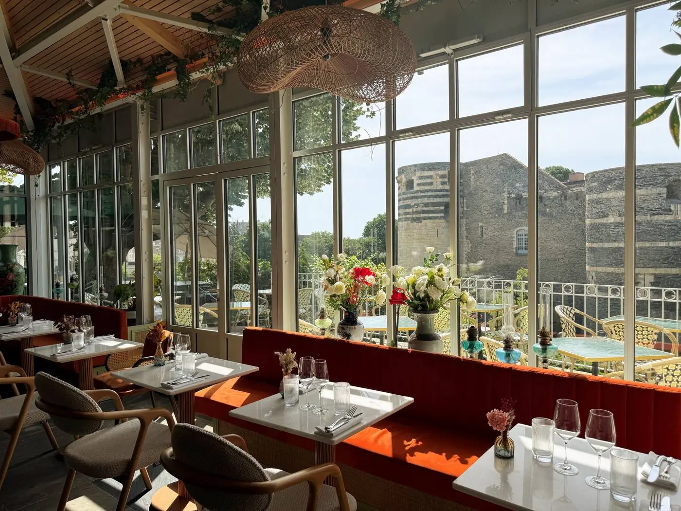 La Verrière de L'Arche : salle vitrée, banquettes de velours orange, tables en marbre et vue directe sur les tours du Château d'Angers